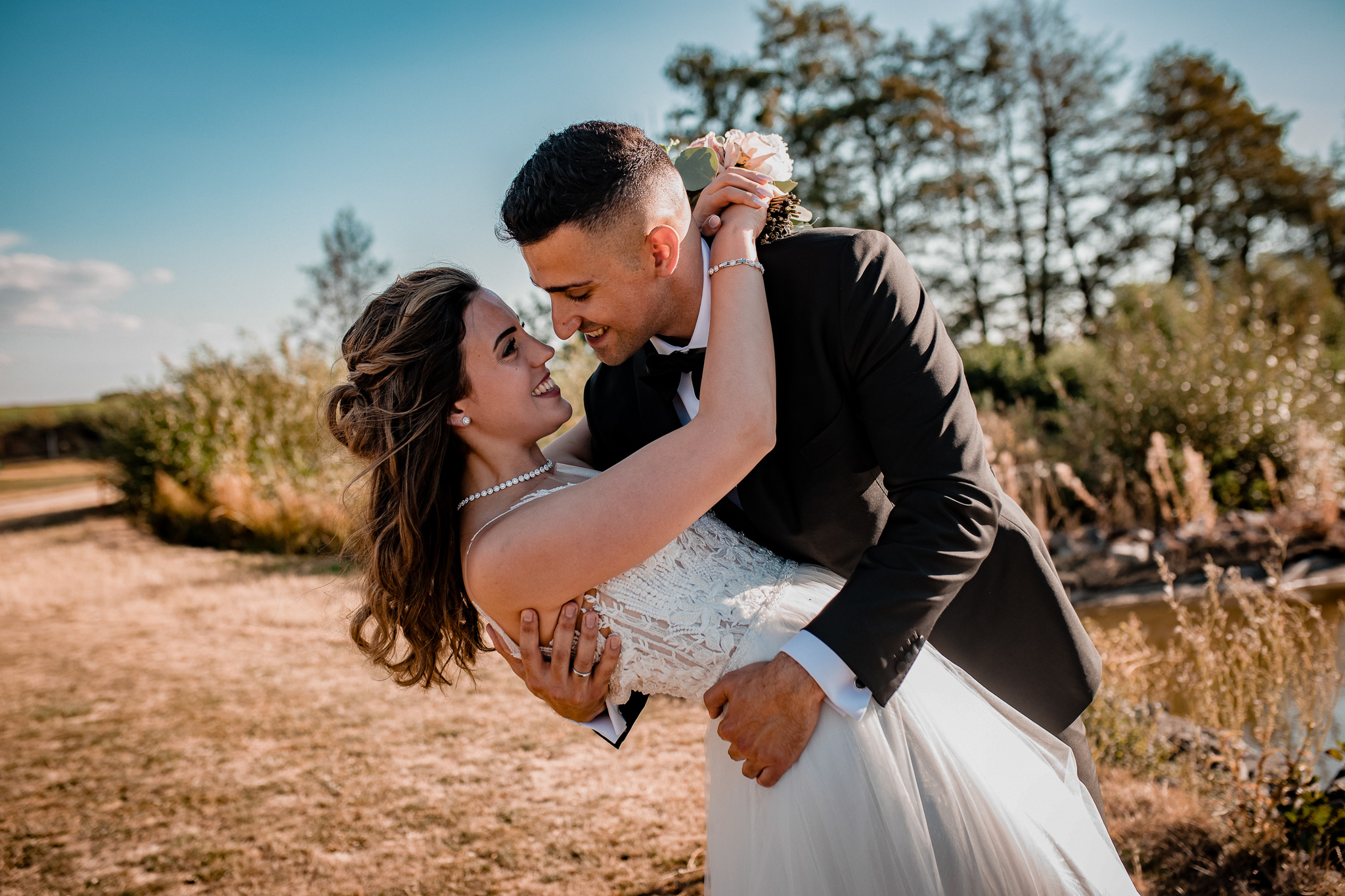 Romantische Szene auf einem Golfplatz bei Sonnenuntergang – der Bräutigam hält seine Braut vollständig in den Armen, beide elegant gekleidet und überglücklich, eingefangen im Hochzeitsvideo Stuttgart.